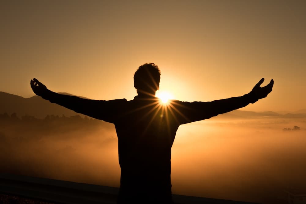 Person standing with open arms toward the sunrise, symbolizing transformation